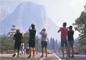  ?? Eric Paul Zamora / Associated Press ?? Visitors photograph El Capitan through a veil of smoke Tuesday after Yosemite Valley reopened. Services remained limited in the park, which was closed for nearly three weeks.