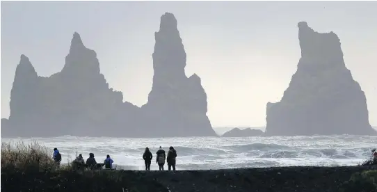  ?? PHOTOS: FRANK AUGSTEIN/THE ASSOCIATED PRESS/FILES ?? People sit on rocks at the black sanded beach in Vik, Iceland, near the Volcano Katla. Iceland is home to 32 volcanic sites.