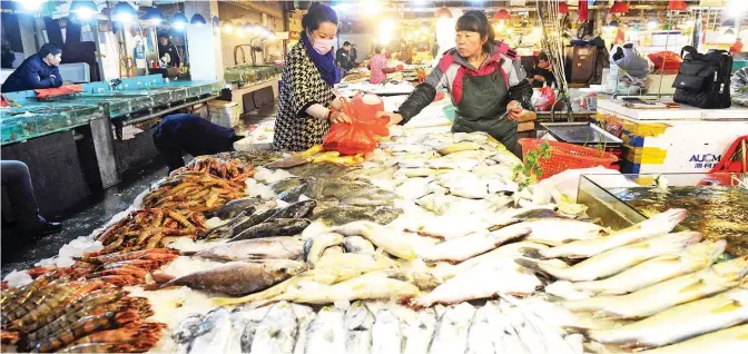  ??  ?? QINGDAO: A customer buying fish at a food market in Qingdao, eastern China’s Shandong province. China’s consumer price inflation fell to a five-month low in October, the government said yesterday. — AFP (See page 23)