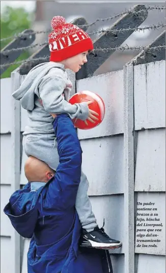  ??  ?? Un padre sostiene en brazos a su hijo, hincha del Liverpool, para que vea algo del entrenamie­nto de los reds.