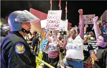  ??  ?? A Phoenix police officer watches as a crowd of protesters outside the Phoenix Convention Centre hold up signs and chant anti-Trump slogans. — AFP photo