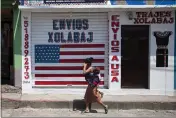  ?? MOISES CASTILLO — THE ASSOCIATED PRESS ?? A woman carrying a child walks past a closed courier business featuring a U.S. flag and the Spanish phrase: “Send to U.S.A” in the largely indigenous town of Joyabaj, Guatemala, where half of the residents depend on remittance­s, almost all from the U.S.