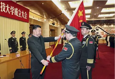  ??  ?? Xi presenting a military flag to officials from the National University of Defence Technology during the ceremony in Beijing. — Xinhua Passing the baton: