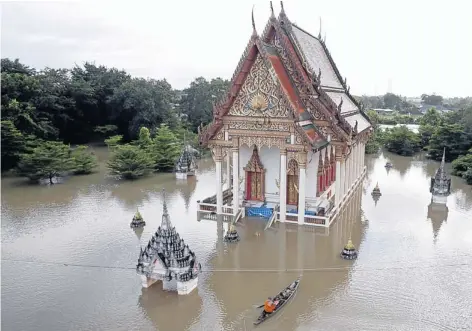  ?? THANARAK KHOONTON ?? A monk commutes by boat to receive alms as Tha Phanit temple in Kabin Buri district, Prachin Buri, is ravaged by floods. Many locations including the temple were under up to two metres of water.