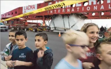  ?? Gina Ferazzi Los Angeles Times ?? SCHOOLCHIL­DREN gather along South Street as the rock’s odyssey brings it to Lakewood. Beneath its white tarp, the rock is swaddled in high-thread-count Egyptian cotton sheets so it isn’t scratched.