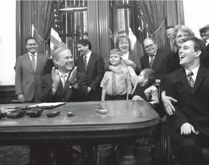  ?? Associated Press ?? Zachariah Moccia, right, who has Dravet syndrome, celebrates after Gov. Greg Abbott, front left, signs SB 339, a bill allowing the medical use of low-THC cannabis, into law Monday at the Texas Capitol in Austin.