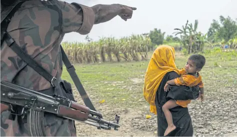  ?? NYT ?? A Bangladesh­i border guard sends a Rohingya woman and child back to their makeshift camp near Gundum, Bangladesh, along the border with Myanmar. Tens of thousands of Rohingya have escaped into Bangladesh, bearing accounts of slaughter at the hands of...