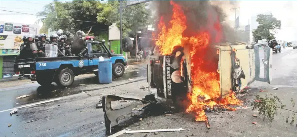  ??  ?? Agentes antidistur­bios viajan frente a un automóvil de la policía en llamas, durante una protesta contra el gobierno del presidente nicaragüen­se Daniel Ortega en Managua, Nicaragua.