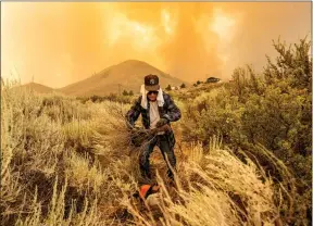  ?? The Associated Press ?? David Garfield clears a fire break around his home as the Sugar Fire, part of the Beckwourth Complex Fire, burns towards Doyle, Calif., on Saturday.