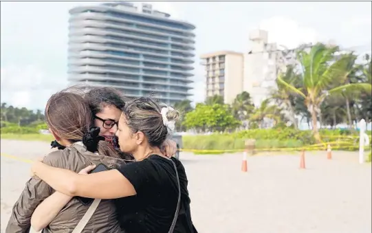  ?? AMY BETH BENNETT/SOUTH FLORIDA SUN SENTINEL PHOTOS ?? Fayzah Bushnaq, center, from Sterling, Virgina, is hugged by Maria Fernanda Martinez, left, and Mariana Cordiero on Friday on the beach in front of the 12-story oceanfront Champlain Towers South Condo in Surfside.