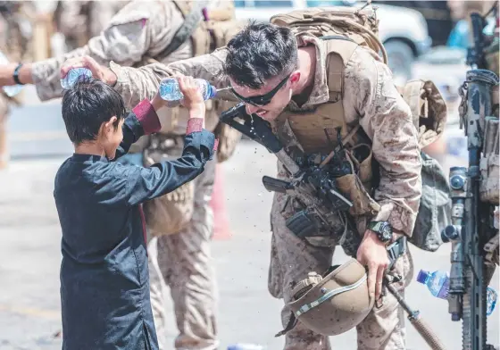  ?? Picture: Getty ?? A US Marine and an Afghan boy spray cold water on each other to cool off as the evacuation of Kabul ramps up in blistering heat.