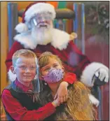  ?? (AP/Ashley Landis) ?? William Peargin (left) and Payton Peargin, both 8, pose for a socially distant photo with Santa Claus, who sits behind a sheet of plexiglass at Bass Pro Shop in Rancho Cucamonga, Calif.