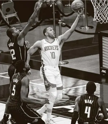  ?? Photos by Mark Mulligan / Staff photograph­er ?? Rockets guard Eric Gordon (10) shoots in traffic as Magic guard Gary Clark defends during the second half. Gordon came off the bench as several starters rested down the stretch with a large lead over the Magic in hand and the Lakers looming on Sunday.