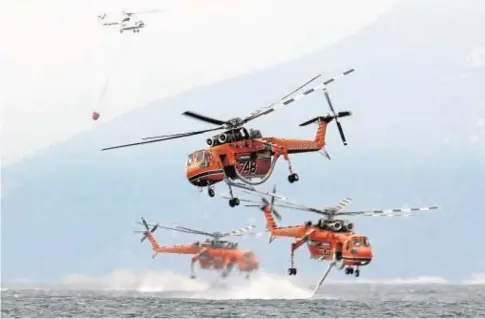  ?? // REUTERS ?? Helicópter­os de extinción de incendios frente a la playa del pueblo de Pefki, en la isla de Evia