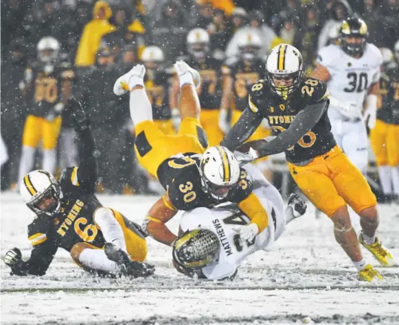  ?? Andy Cross, The Denver Post ?? Wyoming linebacker Logan Wilson tackles Colorado State running back Izzy Matthews during the fourth quarter of Saturday’s Border War game on the snow-covered field at War Memorial Stadium in Laramie. Matthews rushed for 41 yards and a touchdown on 11...