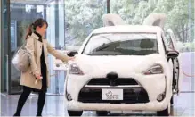  ?? — AFP ?? A woman touches Toyota’s vehicle decorated as shape of dog at its headquarte­rs in Tokyo.