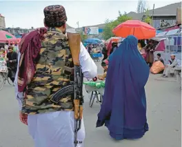  ?? EBRAHIM NOROOZI/AP ?? A woman wearing a burqa walks in the old market Sunday as a Taliban fighter stands guard in Kabul, Afghanista­n. Some Afghans questioned the latest Taliban edit.
