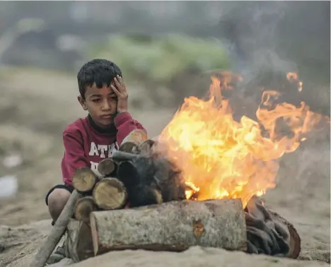  ?? BULENT KILIC/AFP/GETTY IMAGES ?? A boy sits next to a fire Sunday at a makeshift camp set up by migrants stranded by the blockade at the Greek-Macedonian border.