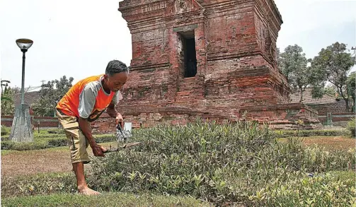  ?? HANUNG HAMBARA/JAWA POS ?? MINIM PENGUNJUNG: Semin, petugas kebersihan, merapikan tanaman di kompleks Candi Pari. Berkunjung ke lokasi wisata religi dan pendidikan kurang diminati.