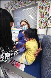  ?? ?? Sanchez places a bandage on the arm of Natalia Adame, 8, after administer­ing the Pfizer vaccine to her at the Kaiser Permanente medical office building Friday afternoon. Natalia’s mom, Rosa Adame, comforts her daughter during the experience.