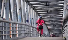  ??  ?? A woman wearing a face mask and a biosafety suit rides her bicycle as she crosses on a bridge at Kennedy in Bogotá in July. Photograph: Guillermo Legaria/Getty Images