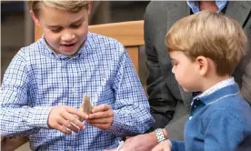  ?? Photograph: Kensington Palace/AFP/Getty Images ?? Prince Louis (right) watching as Prince George holds the giant shark tooth given to him by Sir David Attenborou­gh in the gardens of Kensington Palace.