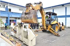  ??  ?? Zaini controls a backhoe loader to ‘crush’ a gambling machine before disposing of it through e-waste method.