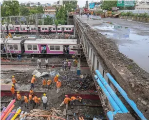  ?? PTI ?? Workers carry out repair work of a foot overbridge that collapsed on the railway tracks on Tuesday at the Andheri station following heavy rains in Mumbai, on Wednesday. Right, a rickshaw puller ferries his passengers through a water-logged street after...