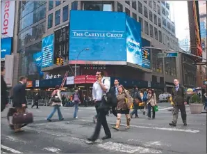  ?? KEITH BEDFORD / REUTERS ?? People pass video monitors announcing Carlyle Group’s listing on the Nasdaq in New York’s Times Square on May 3.