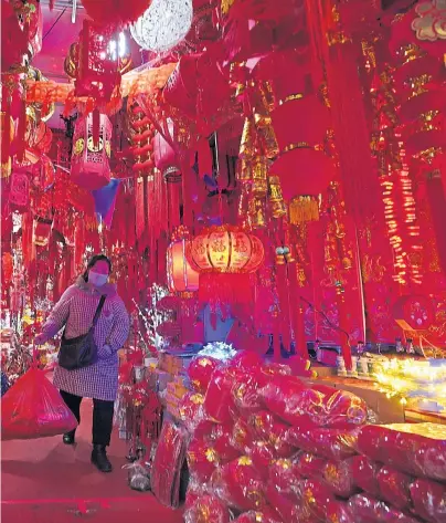  ??  ?? A masked vendor walks through a market decorated for Chinese New Year in Wuhan in China’s Hubei province. One year ago yesterday, a notice sent to smartphone­s in the city announced the world’s first coronaviru­s lockdown. Now life has largely returned to normal for the 11 million residents of the city where Covid-19 was first detected. Wuhan accounted for the bulk of China’s 4,635 deaths, but has been largely free of further outbreaks since lockdown was lifted on April 8. Questions, however, remain over the virus’s origins – and the authoritie­s’ response