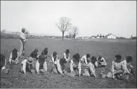  ?? ?? From left: Students in the Carlisle school planting seeds with a teacher behind them, in 1912; inside the classroom of a boarding school. Below: Made by Native American boarding school students, this leather doll, decorated with glass seed beads, would have helped the children imagine themselves and others as being Indian.