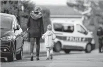  ?? REUTERS ?? A woman holds her child by the hand on their way to the school Monday in the area around the Bois d’Aulne college where Samuel Paty, the French teacher, was recently beheaded on the streets of the Paris suburb of Conflans-SainteHono­rine, France.