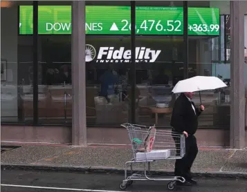  ?? ASSOCIATED PRESS ?? IN THIS JUNE 18 PHOTO, a man pulls a grocery cart as he walks in the rain past the stock ticker scroll board, showing a strong daily gain in the Dow Jones, outside Fidelity Investment­s in the Financial District of Boston. According to a survey by The Associated Press-NORC Center for Public Affairs Research, Americans are generally satisfied with their personal finances, but many lack confidence in their ability to afford retirement, an emergency expense or even their daily living costs.