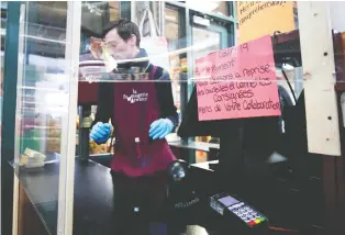  ?? ALLEN MCINNIS FILES ?? A cashier at the Fromagerie in the Atwater Market works behind a proactive Plexiglas barrier as the city deals with the coronaviru­s crisis. Such sights have become the new normal in the COVID-19 world.