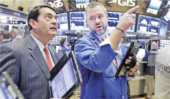  ??  ?? NEW YORK: Traders Mark Muller (left) and Kevin Lodewick work on the floor of the New York Stock Exchange yesterday. Wall Street stocks were little-changed early yesterday following acquisitio­ns by General Electric and CenturyLin­k as markets absorbed...