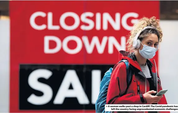  ??  ?? > A woman walks past a shop in Cardiff. The Covid pandemic has left the country facing unpreceden­ted economic challenges