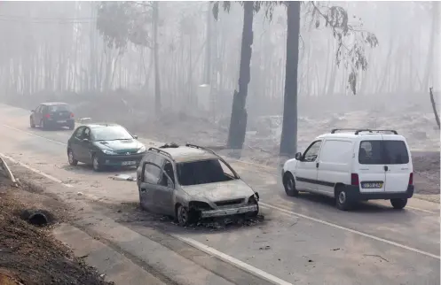  ?? / AP FOTO ?? WILDFIRES. Motorists drive past a burnt car on the road between Castanheir­a de Pera and Figueiro dos Vinhos, central Portugal. Raging forest fires in central Portugal killed more than 50 people, many of them trapped in their cars as flames swept over a...