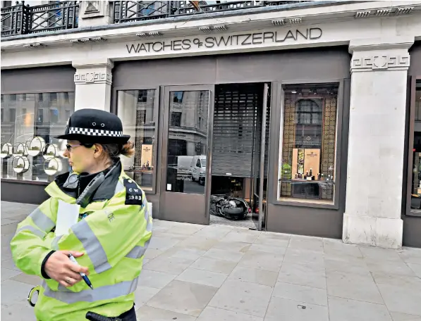  ??  ?? A police officer stands guard at Watches of Switzerlan­d on London’s Regent Street and a scooter can be seen lying inside the store after raiders armed with knives and hammers entered and stole several items of property