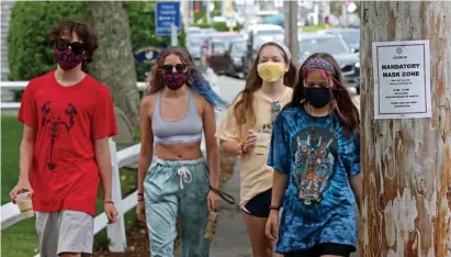  ?? MaTT sTone / Herald sTaff file ?? MASK UP: Teens wearing masks walk down Main Street, passing a sign explaining it’s mandatory to wear masks, on July 1 in Chatham. Cape and Islands officials are worried about an uptick in coronaviru­s cases.