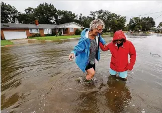  ?? CURTIS COMPTON / CCOMPTON@AJC.COM ?? Anne Herring (right) helps support her friend, Jen Fabrick, as they walk through floodwater­s Wednesday near their homes on St. Marys Street as Hurricane Dorian passes by St. Marys. Fabrick said she is building a raised home in St. Marys with climate change in mind.