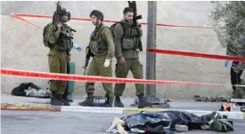 ??  ?? KHIRBIT AL-MISBAH: Israeli soldiers stand next to the body of a Palestinia­n man who was shot dead by security forces at a gas station on a main road between Jerusalem and Tel Aviv yesterday. —AFP
