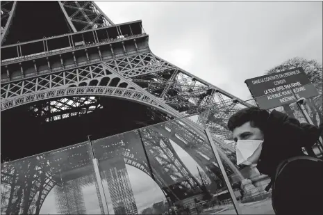  ?? CHRISTOPHE ENA/AP PHOTO ?? A man wearing a mask walks past the Eiffel Tower in Paris on Saturday, closed after the French government banned all gatherings of more than 100 people to limit the spread of the coronaviru­s.