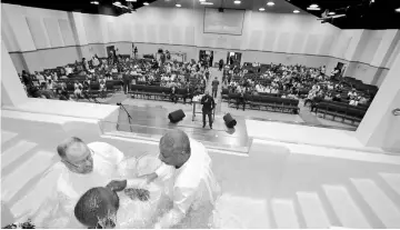  ??  ?? Clifford, left, and Brinkley baptise Corey Bradford at the beginning of the morning service in the multipurpo­se auditorium at Shiloh Metropolit­an Baptist Church in Orange Park, Florida.