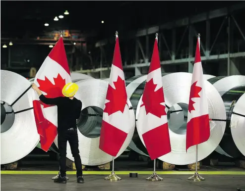  ?? PHOTOS: PETER POWER / THE CANADIAN PRESS ?? A worker straighten­s Canadian flags in front of rolls of coated steel at Stelco in Hamilton before a visit Friday by Foreign Affairs Minister Chrystia Freeland and Economic Developmen­t Minister Navdeep Bains.