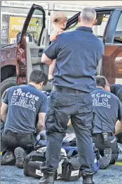  ??  ?? In need of rescue: An emergency worker holds a baby boy as other workers revive a suspected overdose victim at a gas station in Elyria, Ohio.