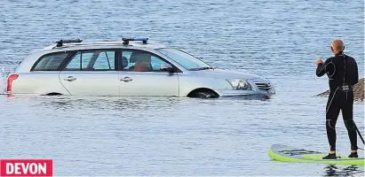  ?? ?? DEVON Parking problem: A paddleboar­der watches a driver trapped by the rising tide in Exmouth