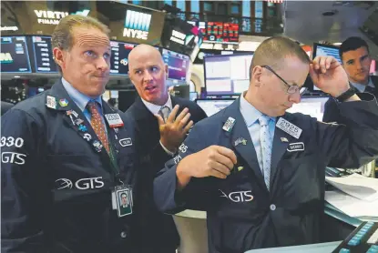  ?? Richard Drew, The Associated Press ?? Specialist­s Glenn Carell, from left, John O’Hara and Robert Nelson gather at a trading post on the floor of the New York Stock Exchange on Wednesday. The Dow Jones industrial average sank 800 points after the bond market flashed a warning sign about a possible recession for the first time since 2007.