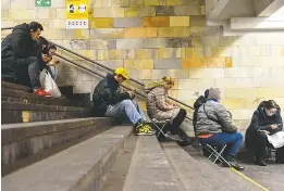  ?? OLEG PETRASYUK/EPA-EFE/SHUTTERSTO­CK ?? TOP: Residents gather near the edge of a crater caused by a rocket strike in Pisochyn, a community in the Kharkiv region of Ukraine. ABOVE: People shelter in the metro system of Kyiv, the Ukrainian capital, after an air raid alert.