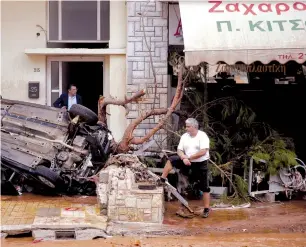  ?? (Alkis Konstantin­idis/Reuters) ?? LOCALS STAND next to a destroyed car following heavy rainfall in the town of Mandra, Greece, yesterday.