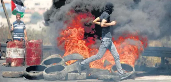  ?? REUTERS ?? A Palestinia­n demonstrat­or runs past burning tyres during a protest over the Israel-gaza tensions, near Hawara checkpoint close to Nablus in West Bank.